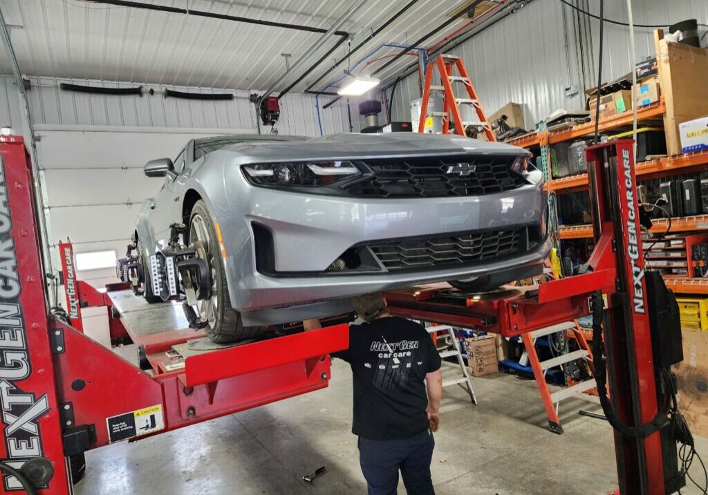 Technician checking the undercarriage of a silver car on lift.